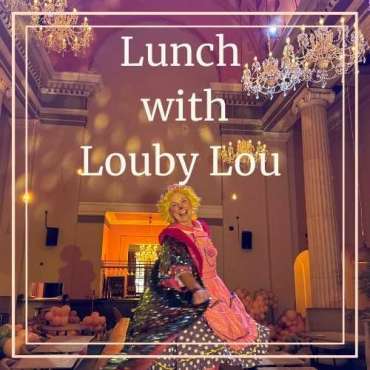 A performer in a vibrant pink costume twirls joyfully beneath ornate chandeliers in a grand, elegant dining hall at Menagerie. Overlaid text reads “Lunch with Louby Lou.”